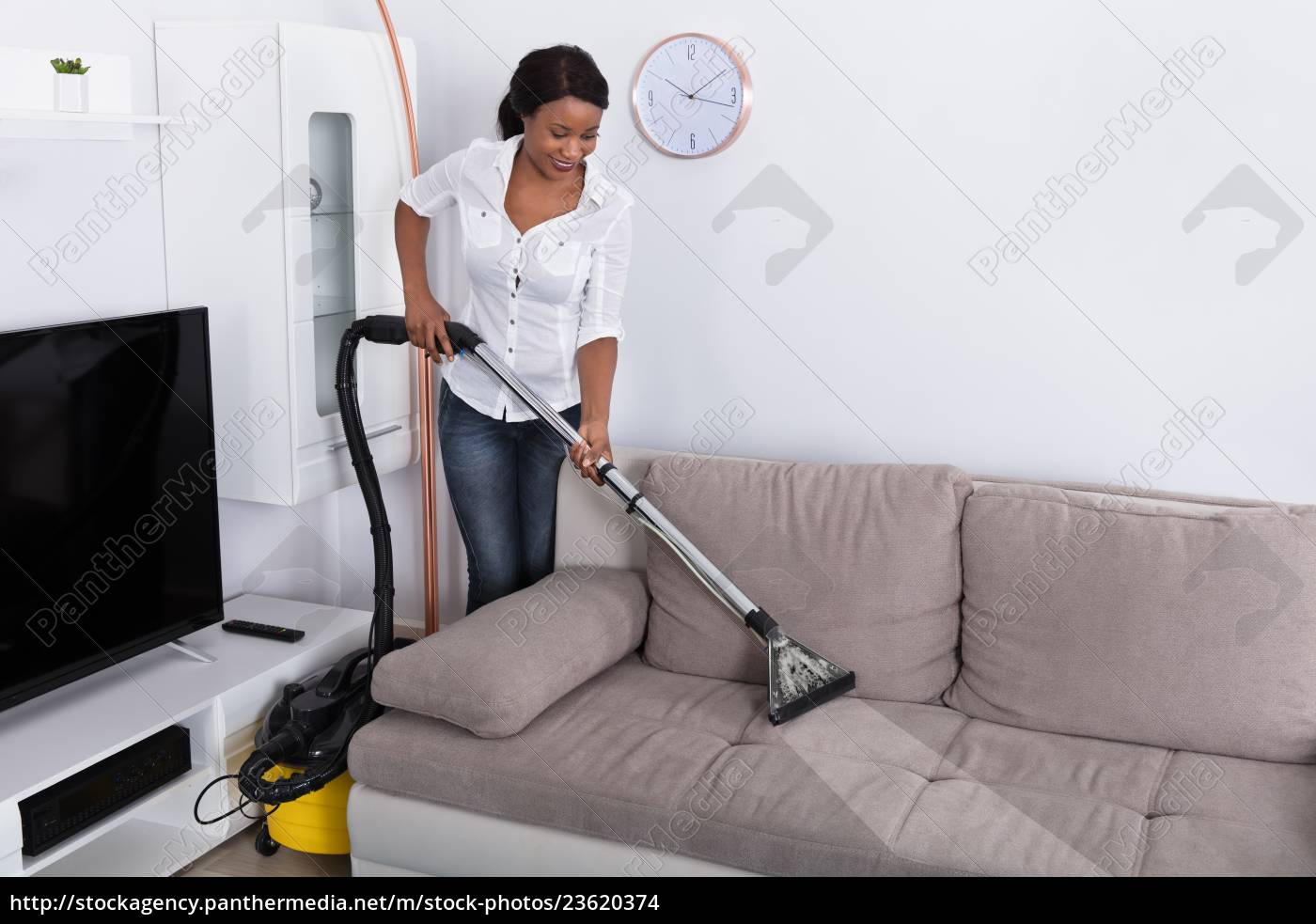 Donna africana che pulisce il divano con aspirapolvere